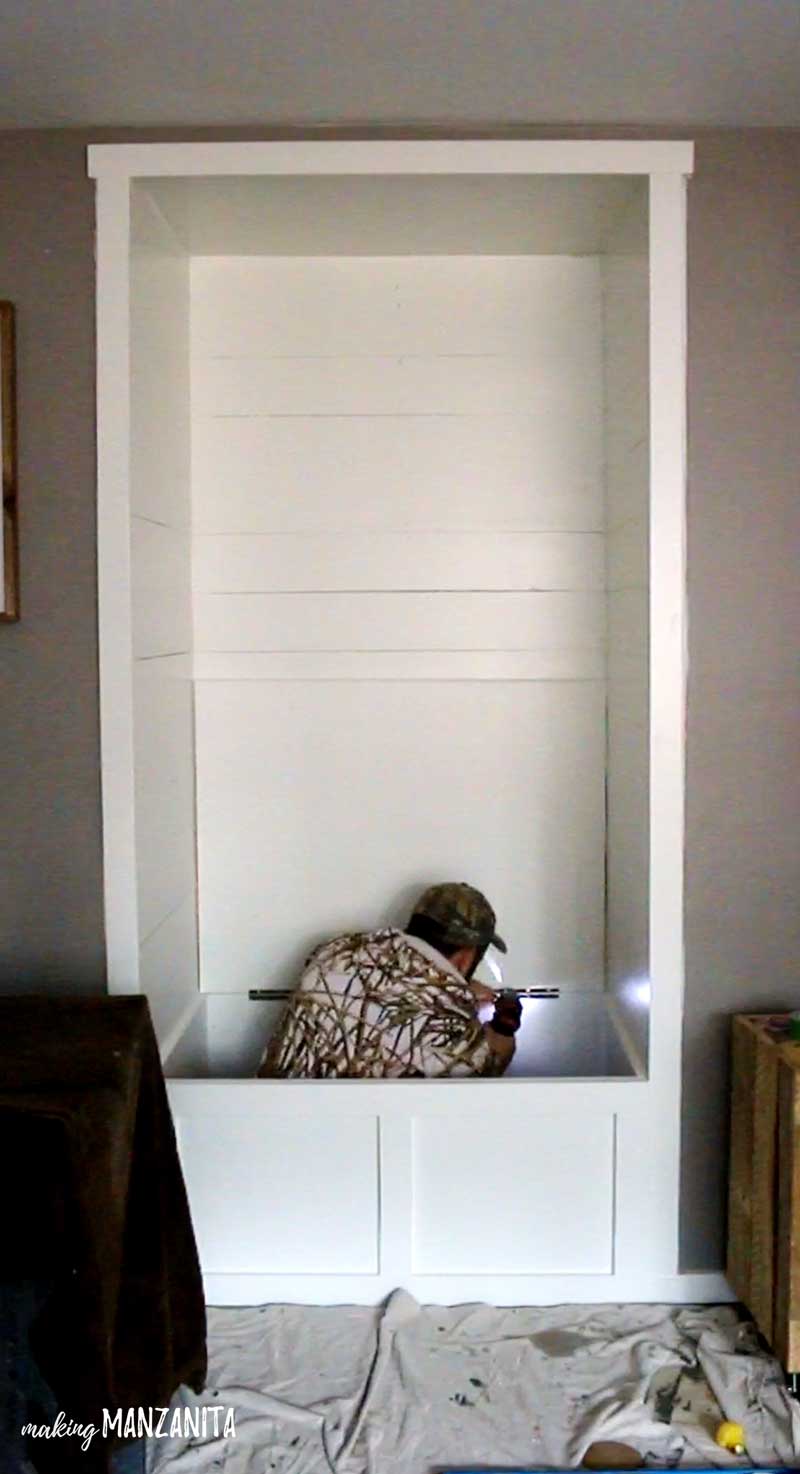 Logan installs the lid of the storage bench in the reading alcove, which has been painted all white.