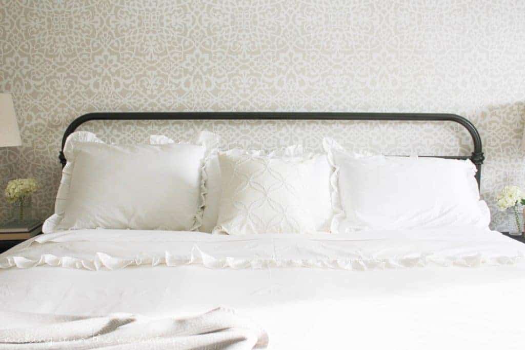 How pretty is this white farmhouse bedding on large iron bed with a stenciled wall behind the bed?