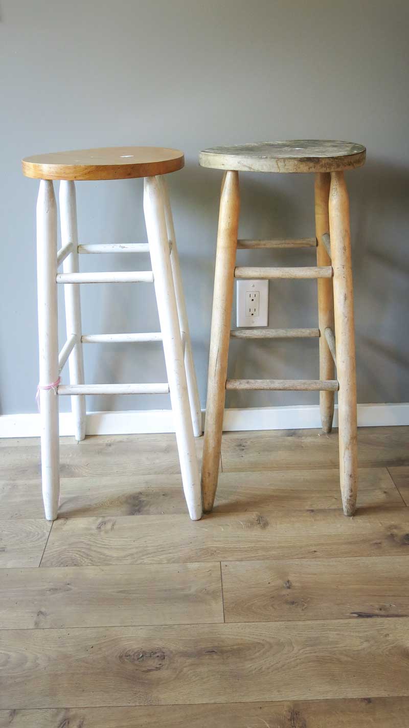 A pair of barstools - one stool is repainted with white wood legs and a dark stained seat. The second still is unpainted, awaiting it's makeover into a stool bedside table