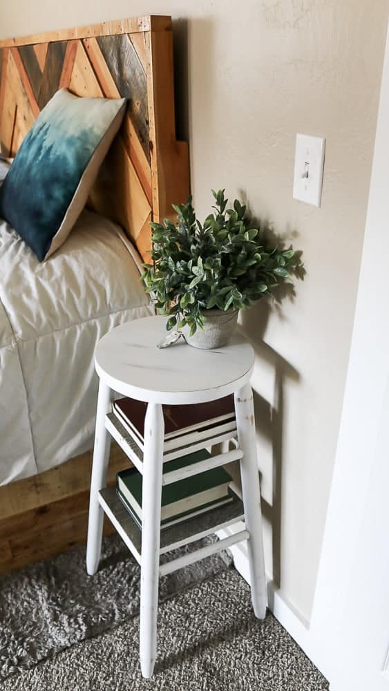 Using the upcycled bar stool as a bedside table to store books and a faux potted plant.