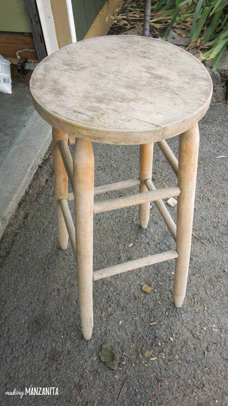 Un unpainted wooden barstool sitting outside. See how we upcycled this barstool into a stool bedside table