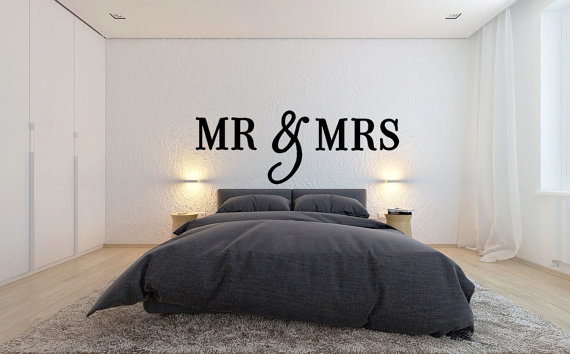 How pretty is this white modern looking bedroom with a gray bed, large white wall behind the bed with wall sign with large letters that says Mr & Mrs ?