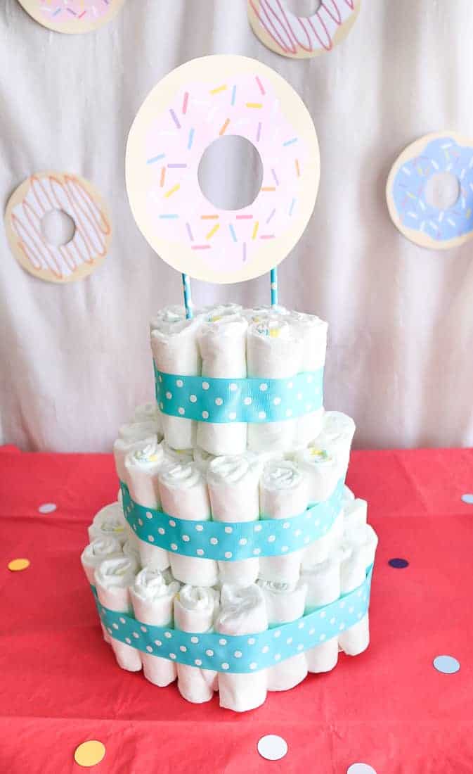 3 Tiered Baby Shower Cake made from diapers with a paper donut topper and blue and white ribbon sitting on a pink table