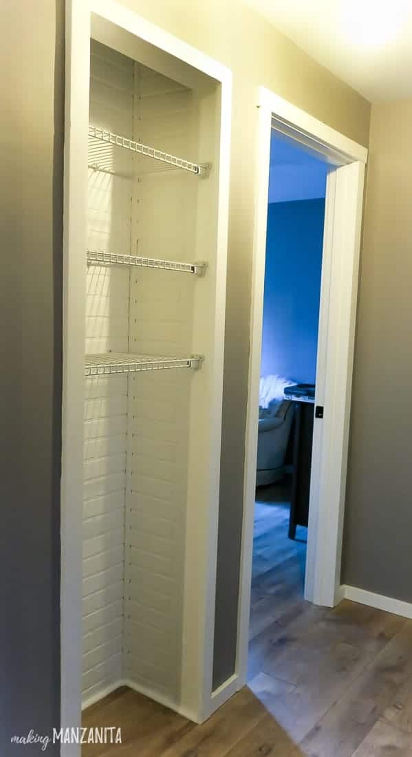 The linen closet in our hallway, updated with a new modern look. The door is removed, the interior is painted white with shiplap walls, and there are three wire shelves hung in the top half of the closet.