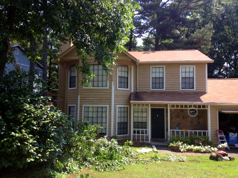 This photo shows tree trimmings on the ground in the front yard of a 2-story home.