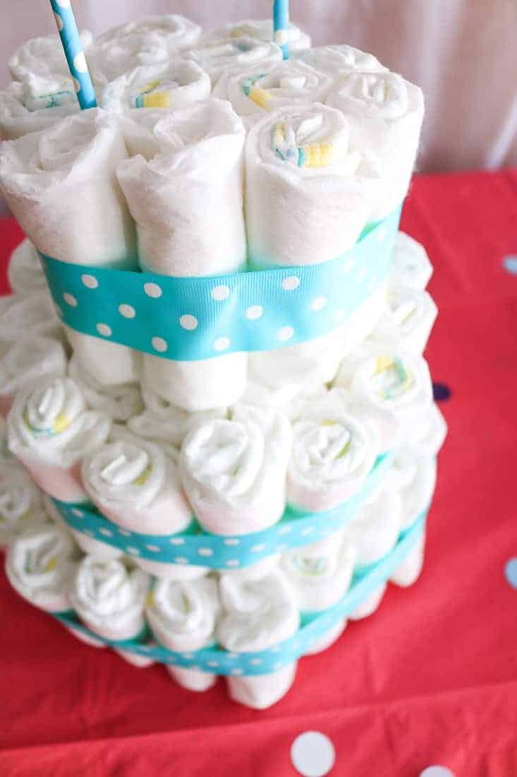 3 tiered cake made with rolled up diapers with polka dot ribbons sitting on pink table