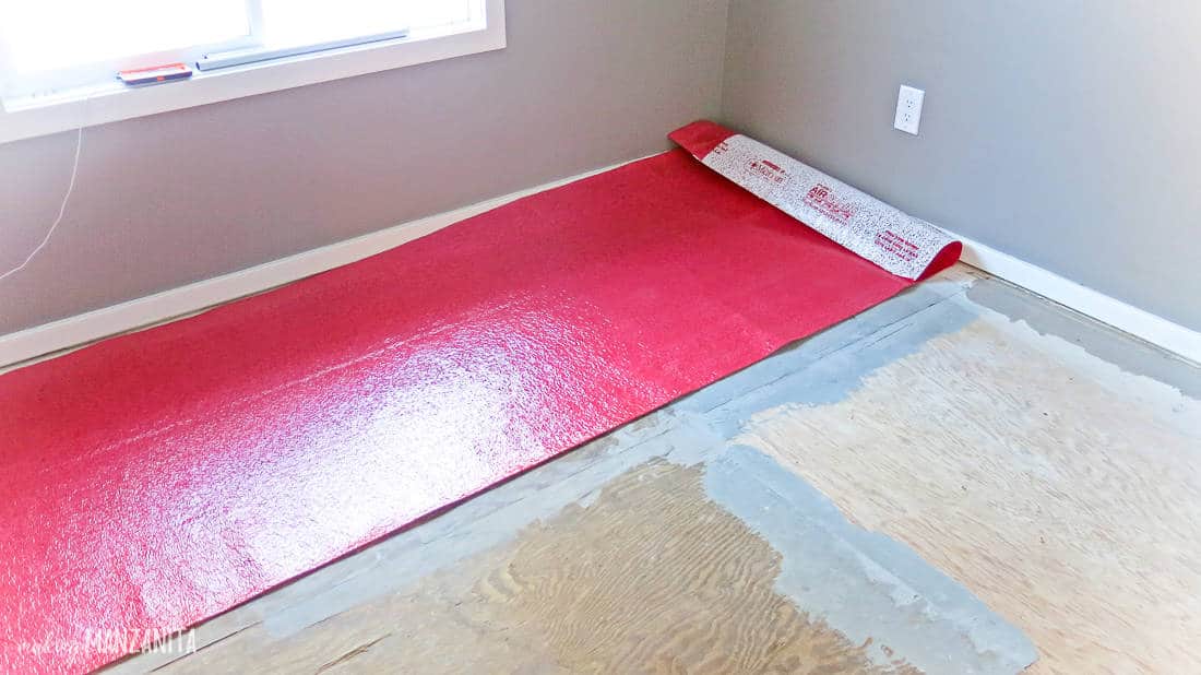 A strip of red flooring padding sits on top of plywood flooring in a gray-painted room.