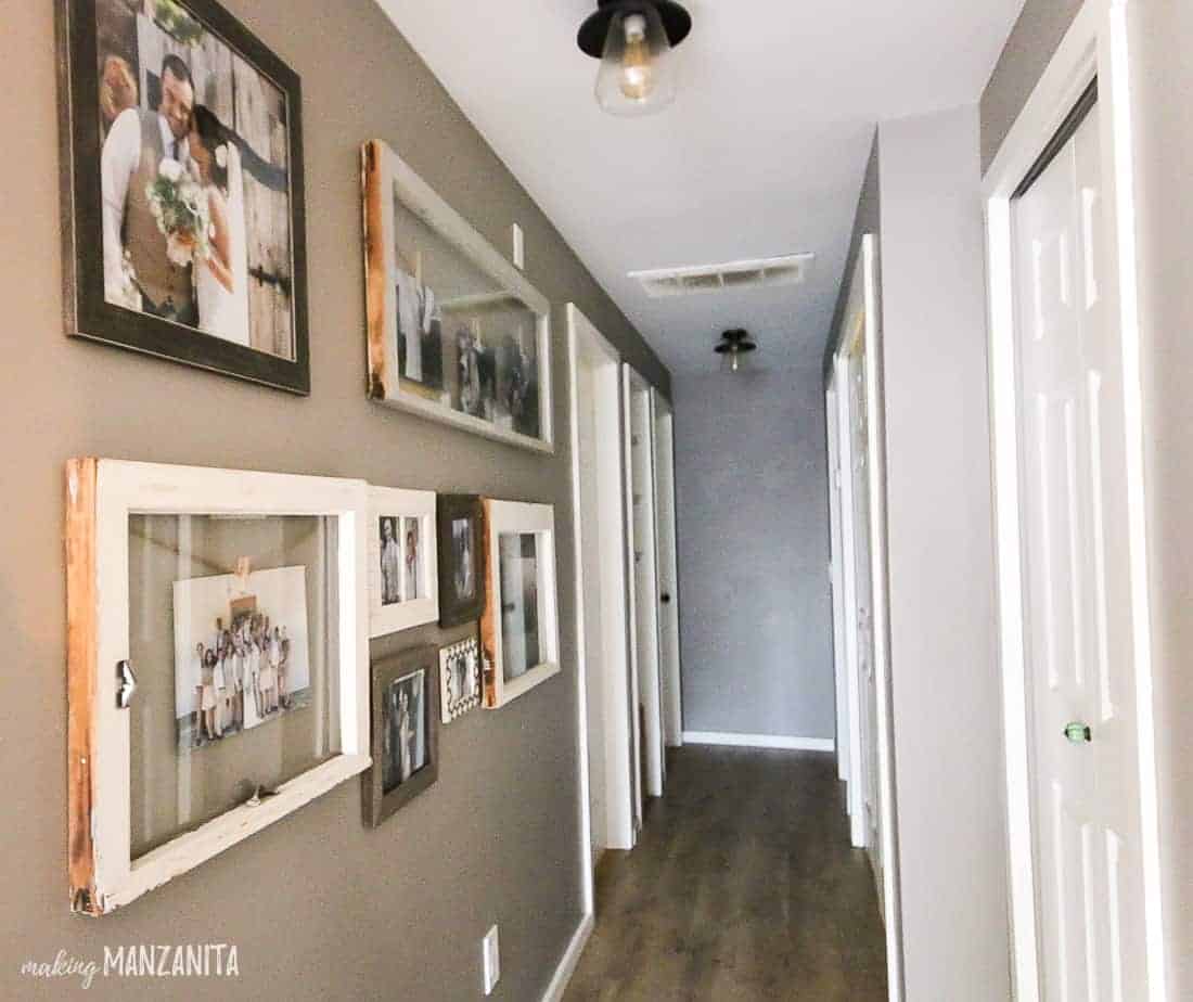 The newly renovated hallway in our home has hardwood flooring, painted walls filled with rustic framed family photos, and updated farmhouse-industrial style light fixtures.