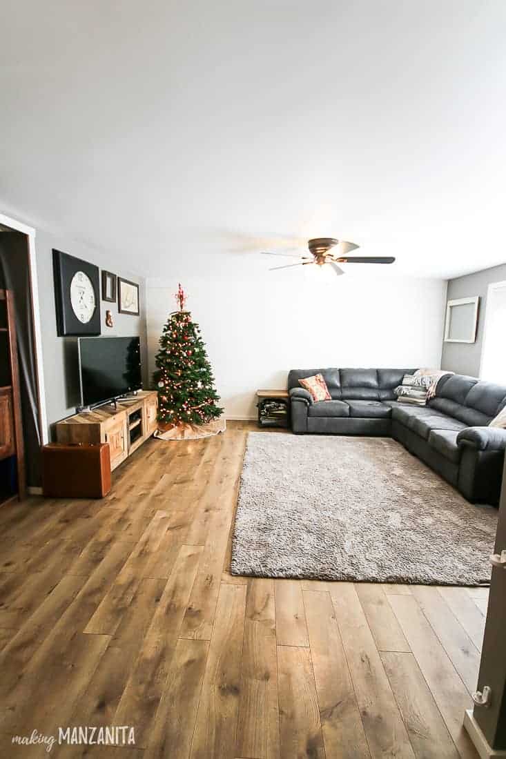 Our living room decorated for Christmas, with a Christmas tree, entertainment center, large area rug, and our large gray faux leather sectional sofa.