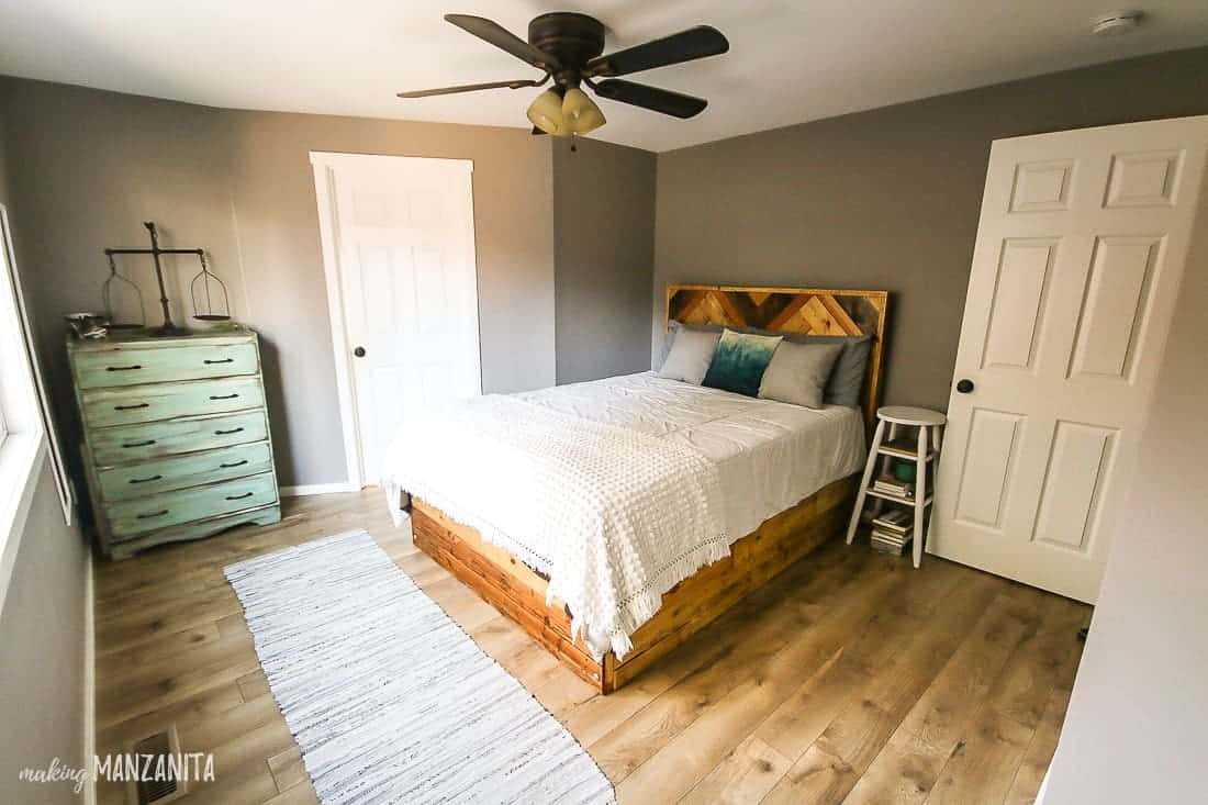 The updated master bedroom features painted walls, a brand-new rustic wooden bed and headboard, hardwood flooring, and a new ceiling fan.