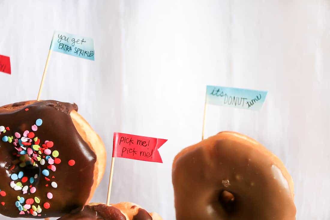 Mini flags made with toothpicks and washi tape, stuck into donuts at the baby shower dessert table, all with cute donut-themed sayings on them