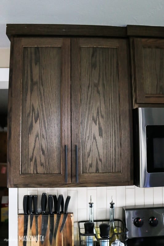 Dark wood upper kitchen cabinet that goes all the way to the ceiling with sleek and modern black cabinet handles 