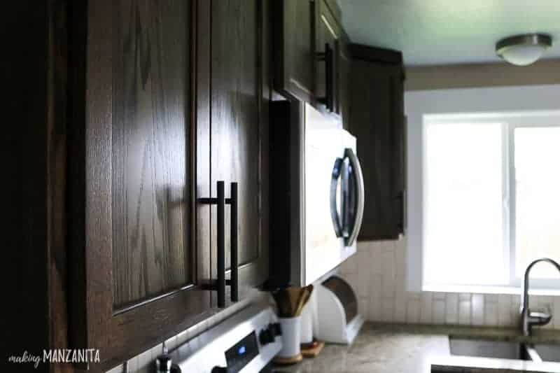 View of upper kitchen cabinets with dark wood stain and modern farmhouse cabinet pulls looking towards kitchen sink and window