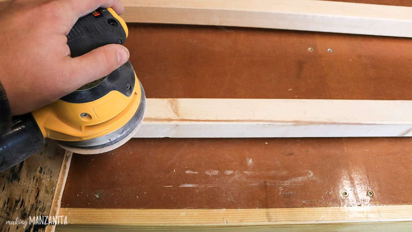 Using an orbital sander to sand down the wood pieces for the baby blanket ladder.