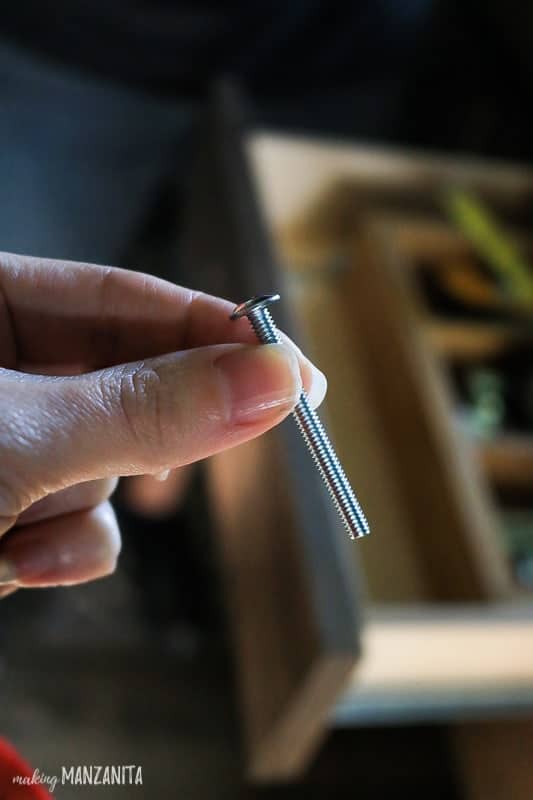 Hand holding longer screw to be used to install cabinet hardware on drawer