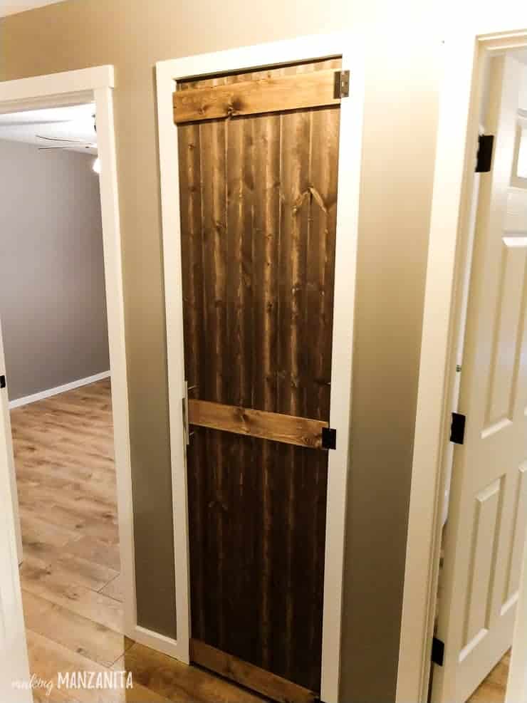The updated hallway closet, now covered with a wooden farmhouse-style door that's been stained a deep chestnut brown color.
