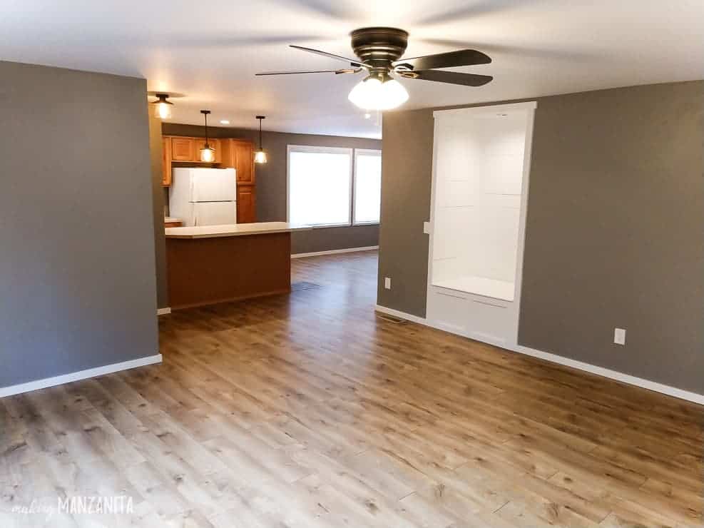 The renovated living room looking into the kitchen -- the room now has hardwood floors, gray walls, and a new reading nook against the far wall.
