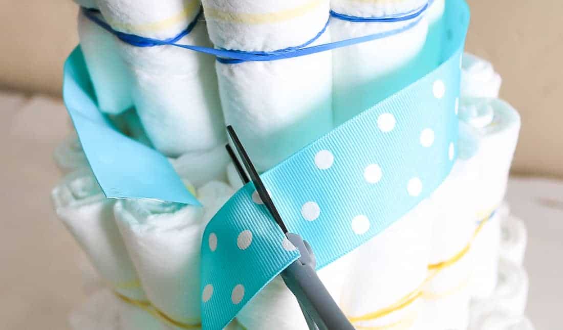 Cutting teal and white polka dot ribbon around a diaper cake for baby shower