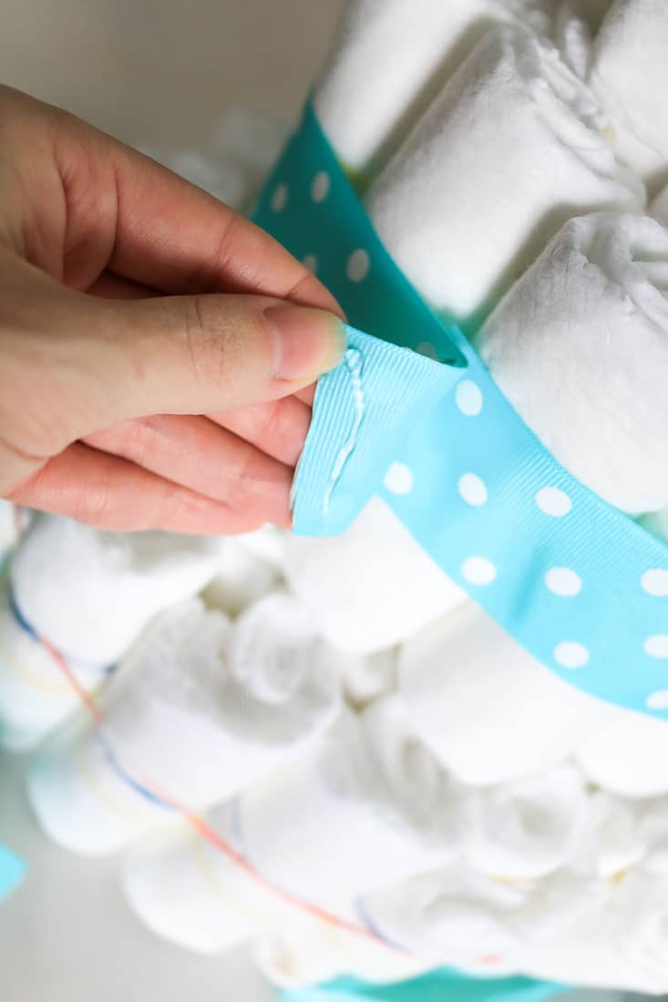 Hot glue to attach teal and white polka dot ribbon to diaper cake