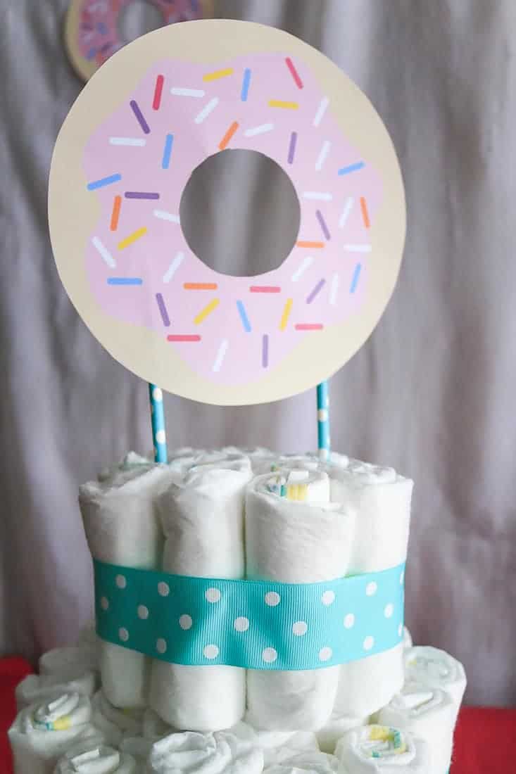 Paper donut taped to straws in the top of a cake made from diapers for a baby shower gift idea