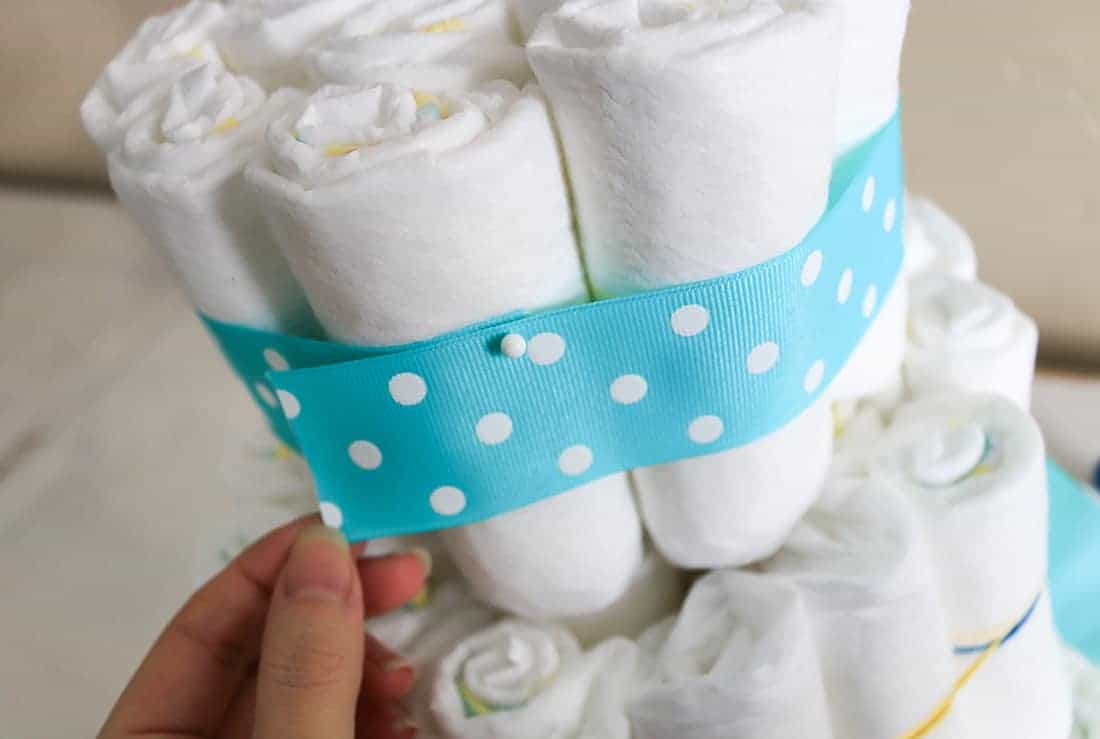 Attaching teal and white ribbon to diaper cake with straight pins to cover up rubber bands