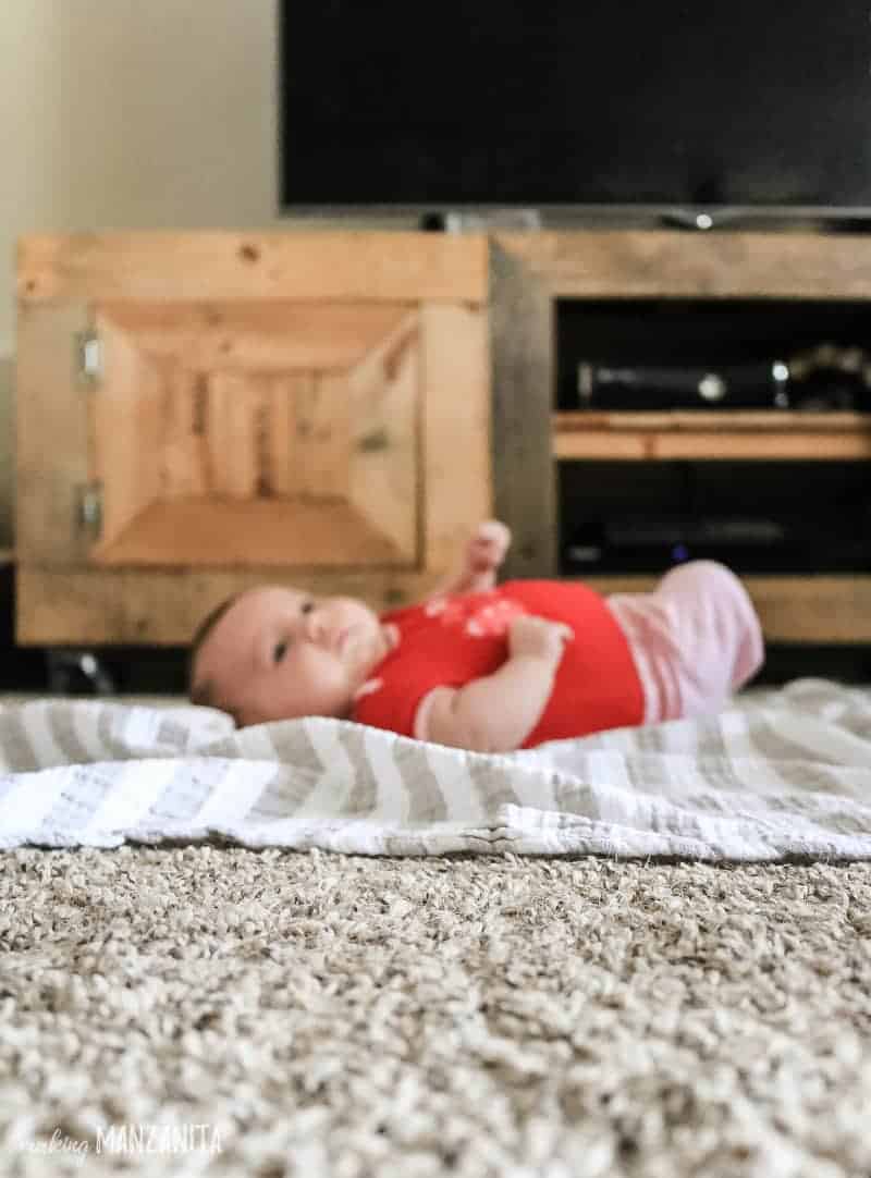 Baby laying on blanket on floor in front of wood entertainment center