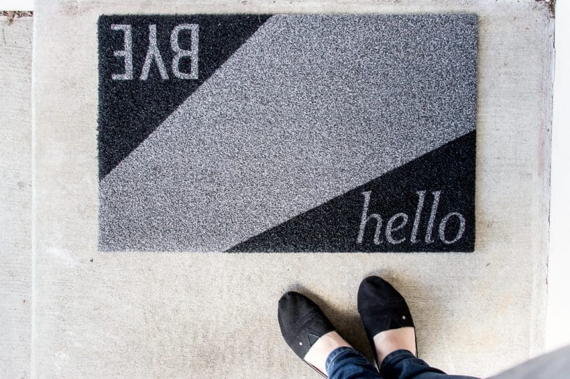 This modern DIY doormat painted with black and gray paint; stenciled on each corner are the words "hello" and "BYE".