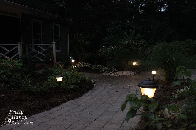 Landscape lights are is a simple way to improve your front or backyard landscaping. This walkway is lit with solar-powered lanterns installed on either side of a paved walkway.