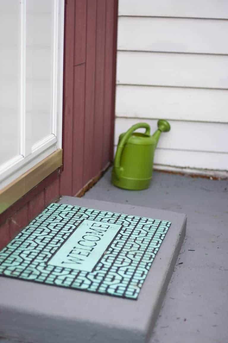A welcome mat painted bright teal sits on a front door stoop. 