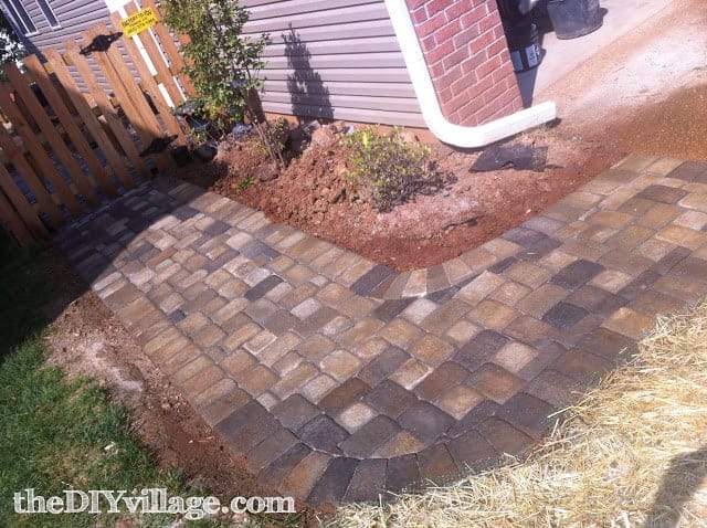 Adding a paved walkway is a simple front yard landscaping tip that improves the look of the exterior of your home. This neutral toned cobblestone walkway leads from a driveway to a fence on the side of the home.