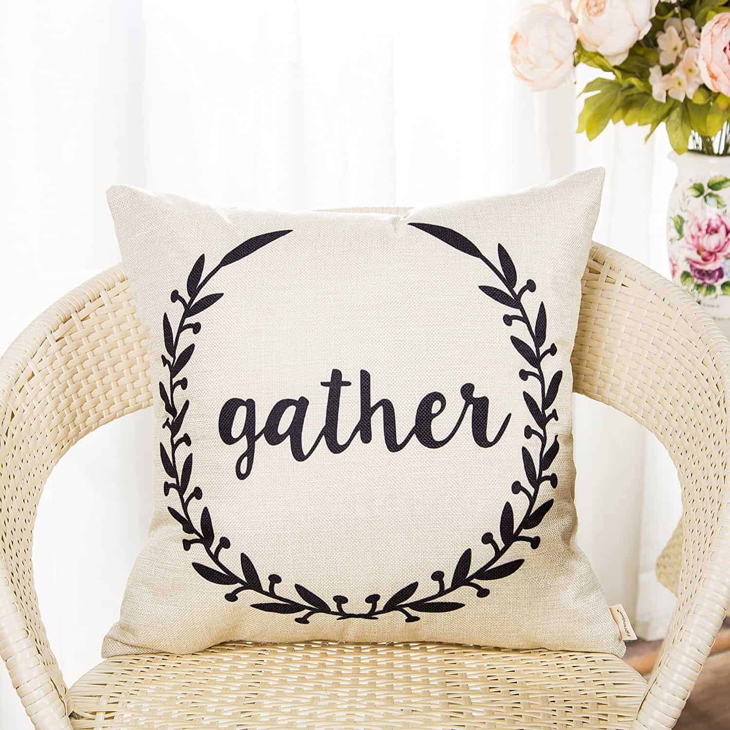 A farmhouse style throw pillow with the word "gather" surrounded by laurel branches