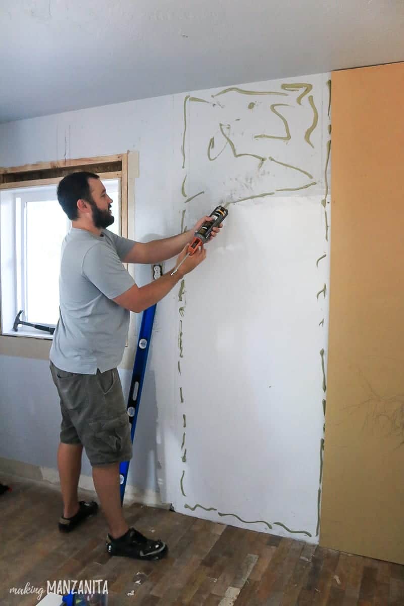 Man applying construction adhesive to wall before adding MDF panel for the back of a board and batten accent wall