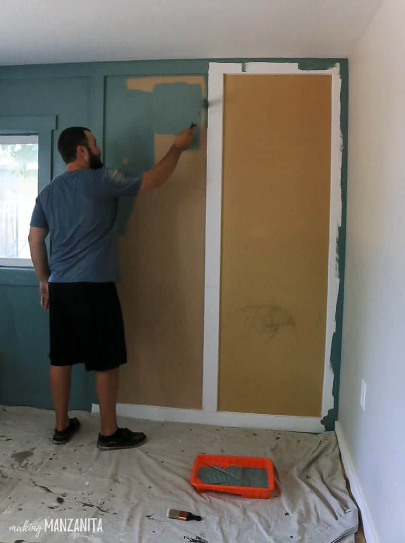 Man painting board and batten feature wall with blue green paint and paint roller