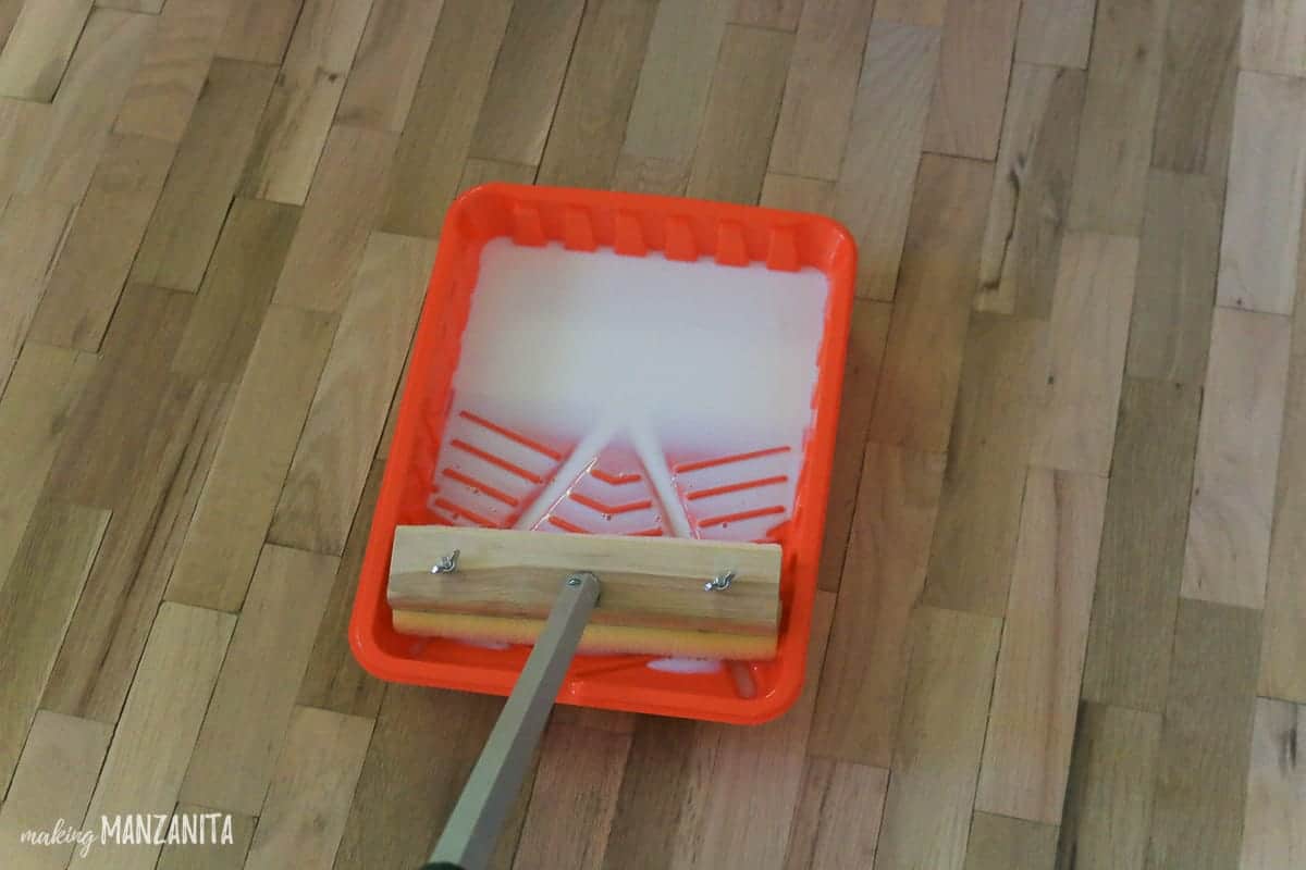 Hardwood floor finish sits in an orange paint tray with a floor finish wood block applicator to apply the finish to the hardwood floors.