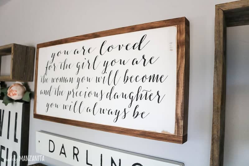 A boho farmhouse sign as the centerpiece of a baby girl's nursery gallery wall