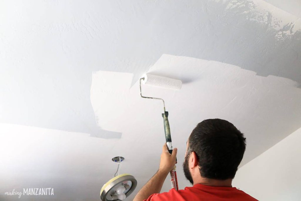 Man rolling white paint onto ceiling with paint roller 