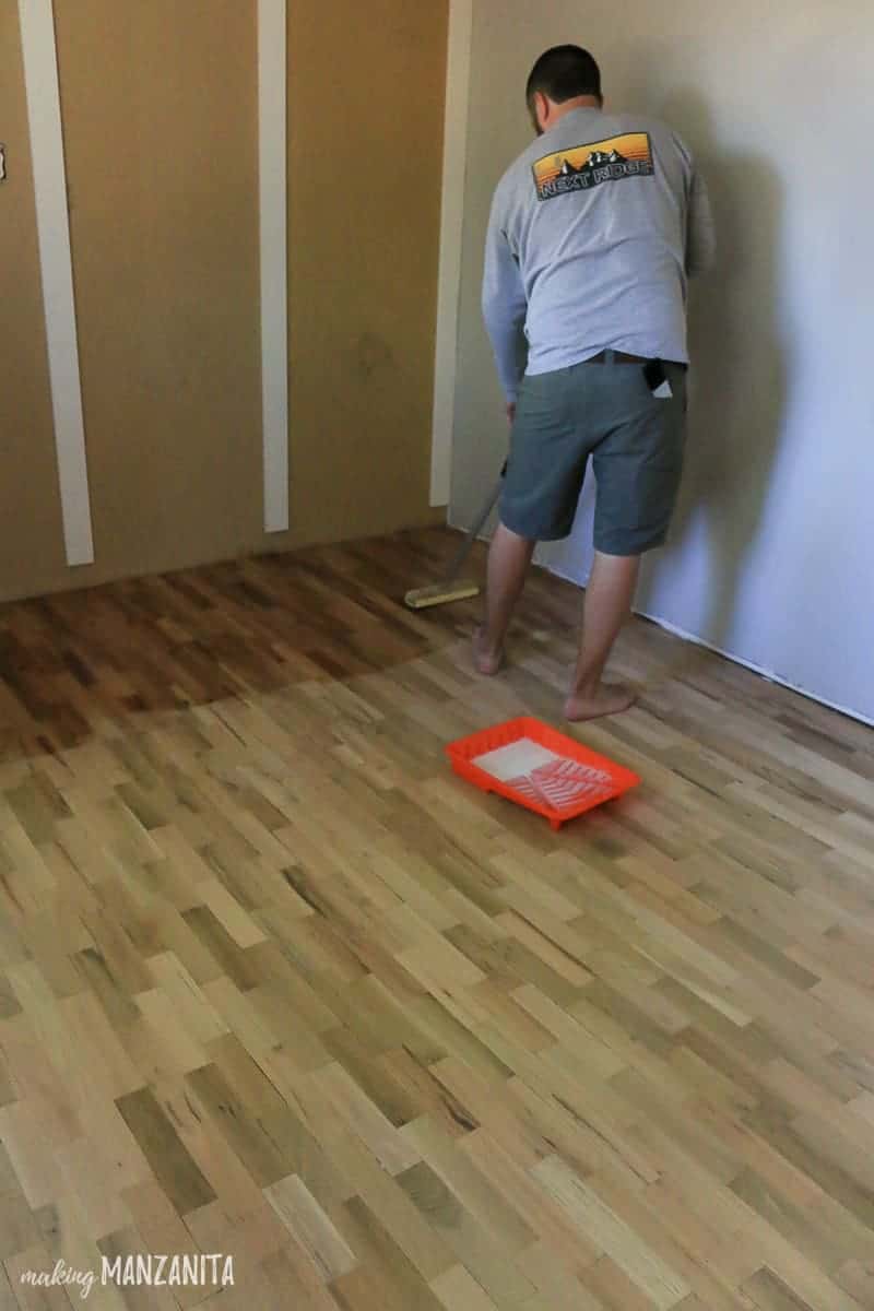 Using a floor finish wood block applicator to apply the floor finish to the sanded and cleaned hardwood floors.