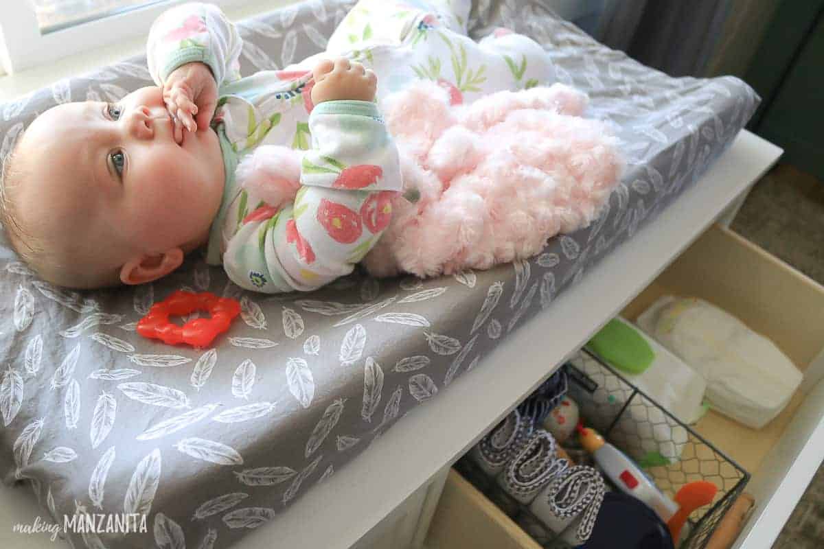 Baby laying on a changing table with organized changing table supplies in an open drawer