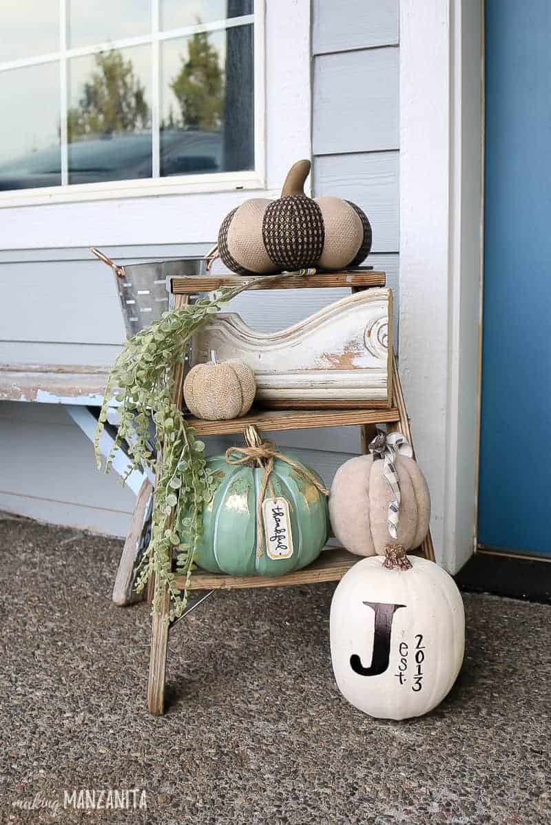 Farmhouse style front porch decorations on antique wooden latter with white pumpkin decor and greenery