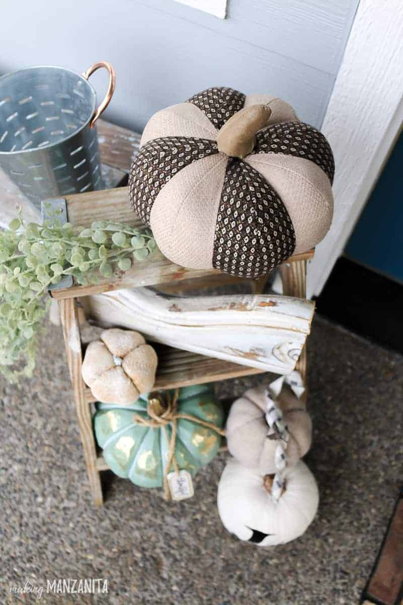 Top view of a wooden ladder covered with faux white pumpkin decor, greenery and white painted corbel