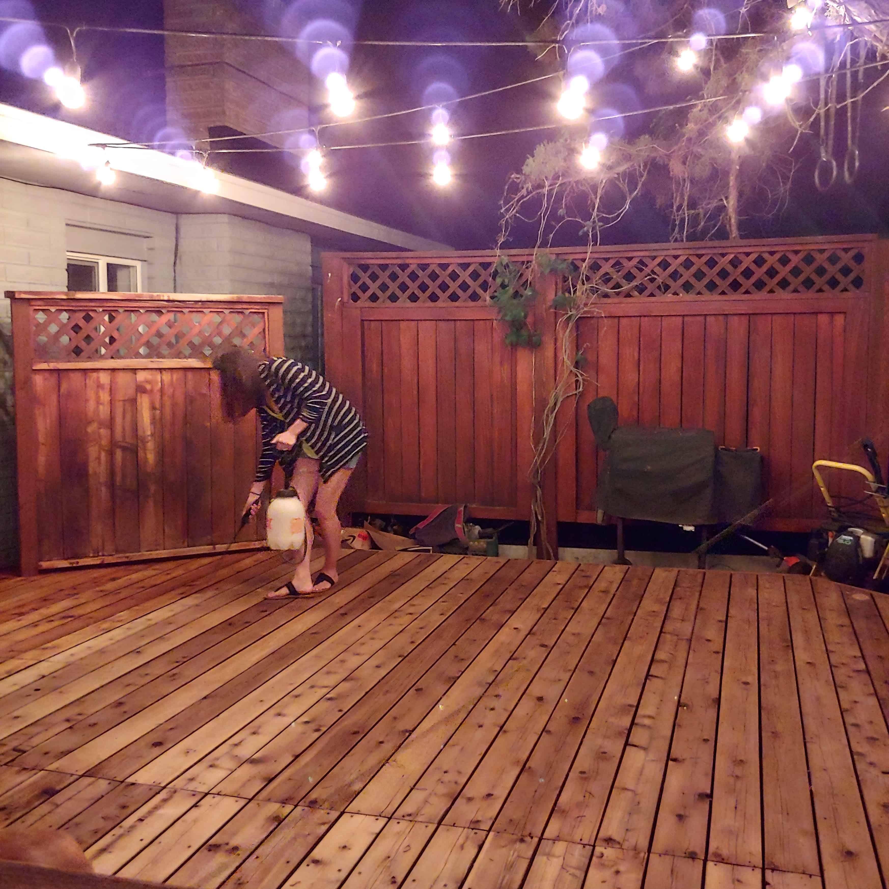 Girl applying wood brightener to wood decking in backyard
