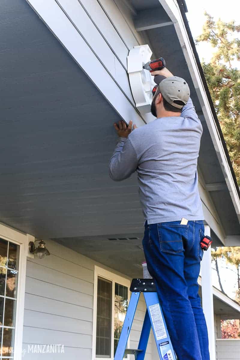 Logan stands on a ladder, installing a decorate louvre to the front gable of our home.