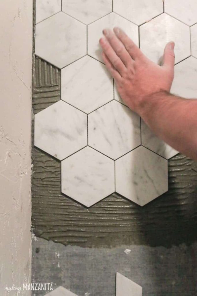 Man pressing down hexagon marble tile with hand over thin set mortar on floor