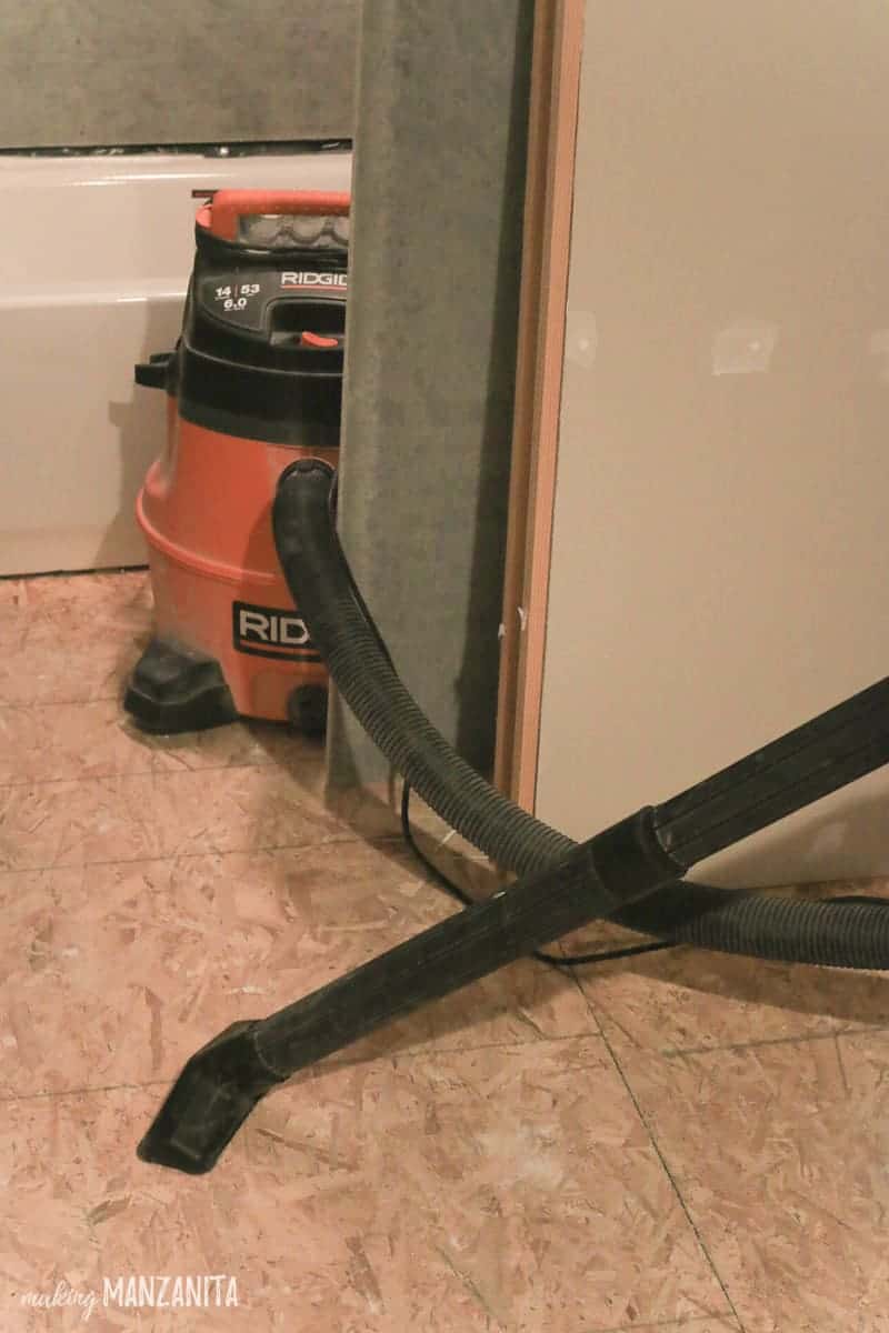 Using a Shopvac to clean dust and debris off the particle board subfloor during a bathroom renovation.