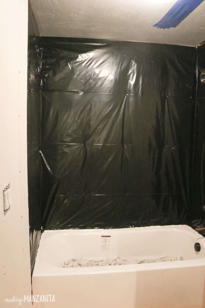 In the middle of our bathroom renovation; a large black plastic sheeting hangs around tub on studs to waterproof a shower