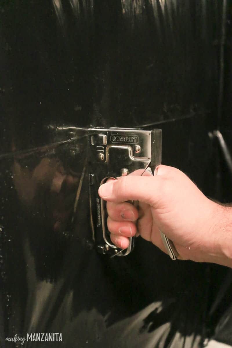 Using a staple gun to attach large plastic sheeting around a tub for waterproofing during a bathroom renovation.