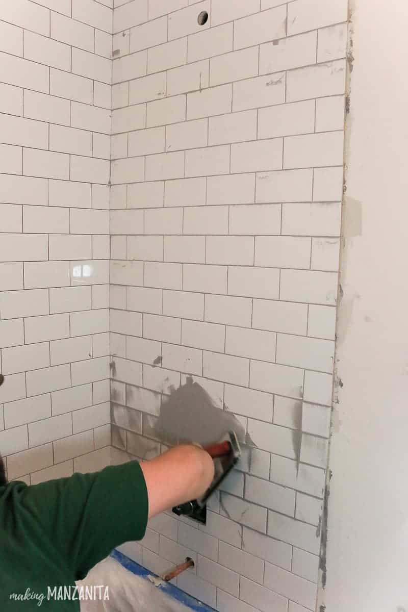 Man spreading gray grout over white subway tile in shower with rubber float 