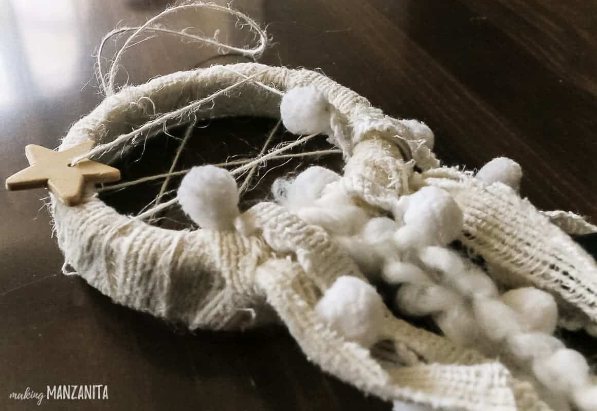 A close up look at the fabric details on the mini dreamcatcher ornament; hanging pieces of fabric with baubles and string.