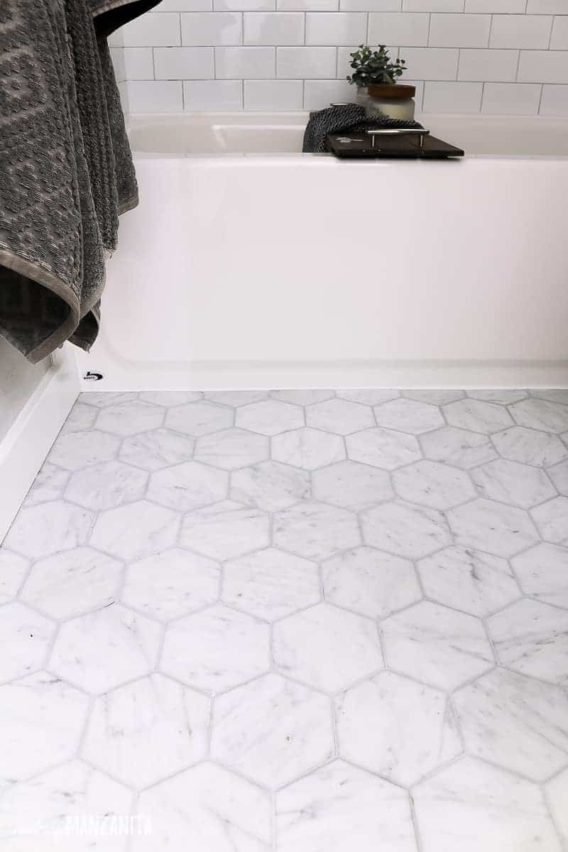 White marble bathroom tile flooring with gray grout in front of a farmhouse bathtub 