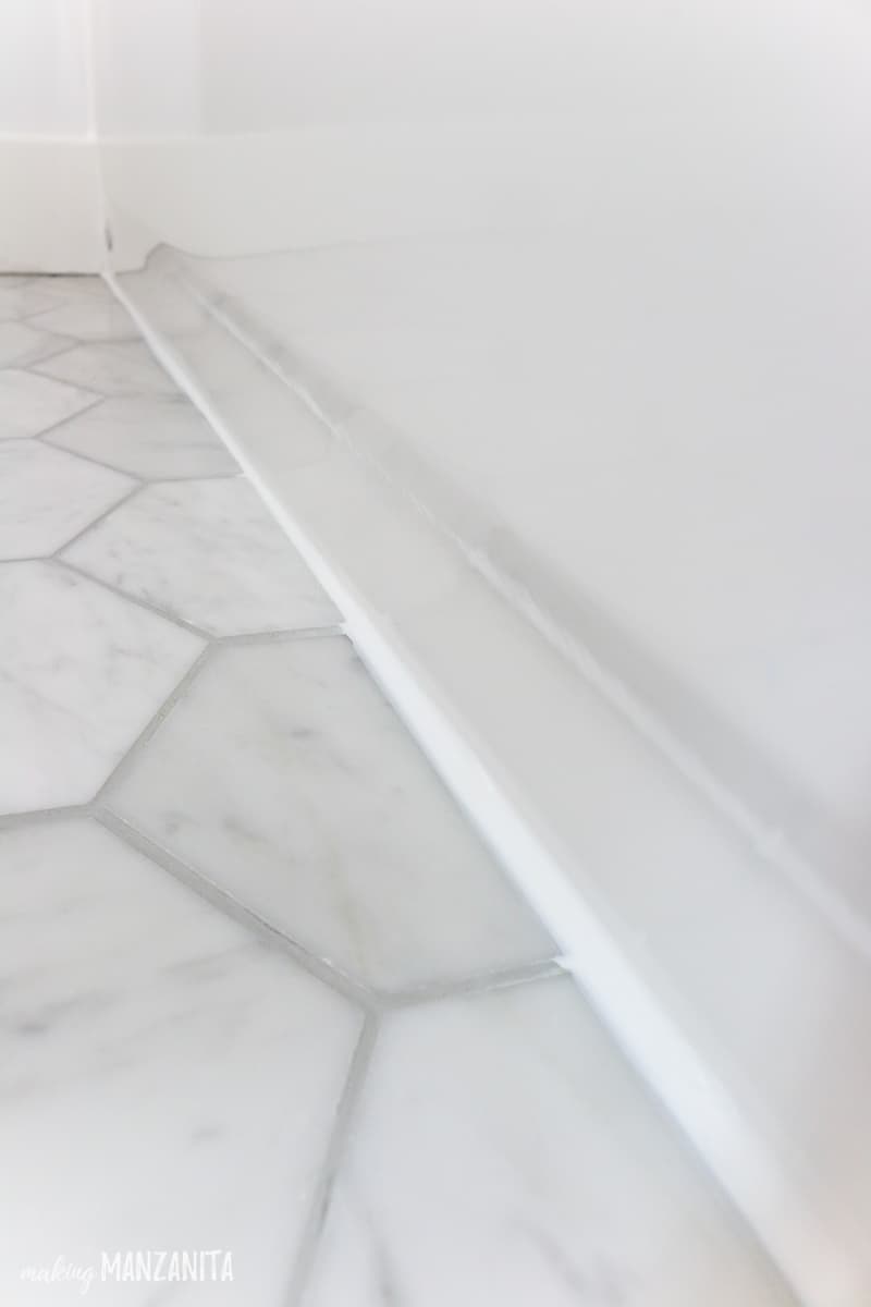 View of where marble floor tile meets the bathtub filled with white caulk to waterproof a shower